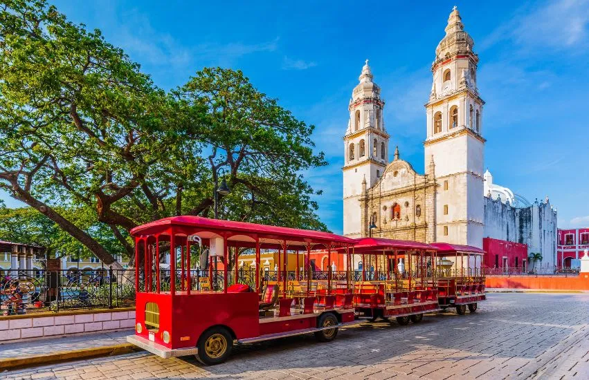 a red trolley with many seats on a street with a white building in the background