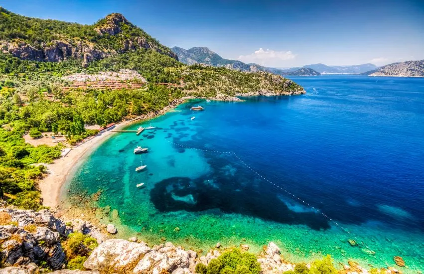 Eine Bucht mit hellblauem Wasser mit Booten und Bergen im Hintergrund. 
